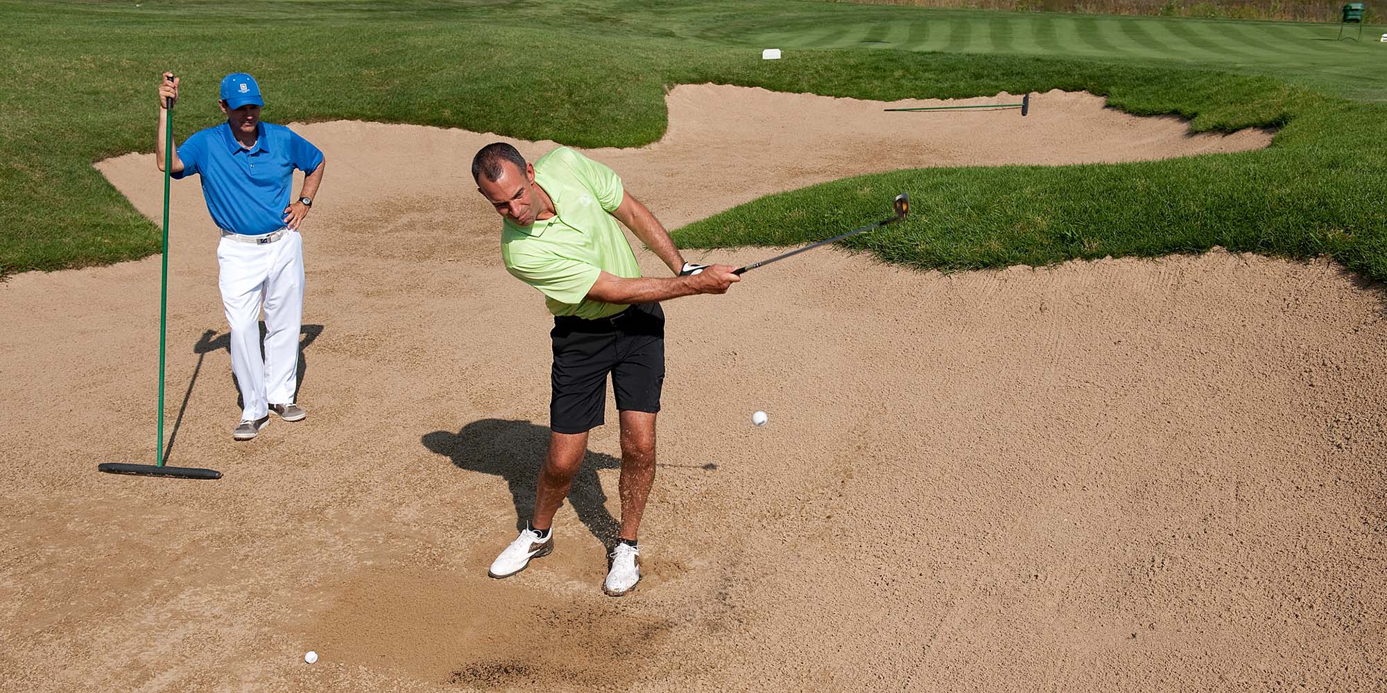 Adult golfer practicing a swing with instructor nearby